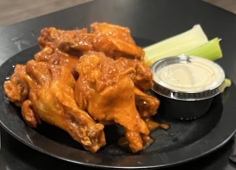 バッファローウィングとカップに入ったランチソース、付け合わせのセロリの写真